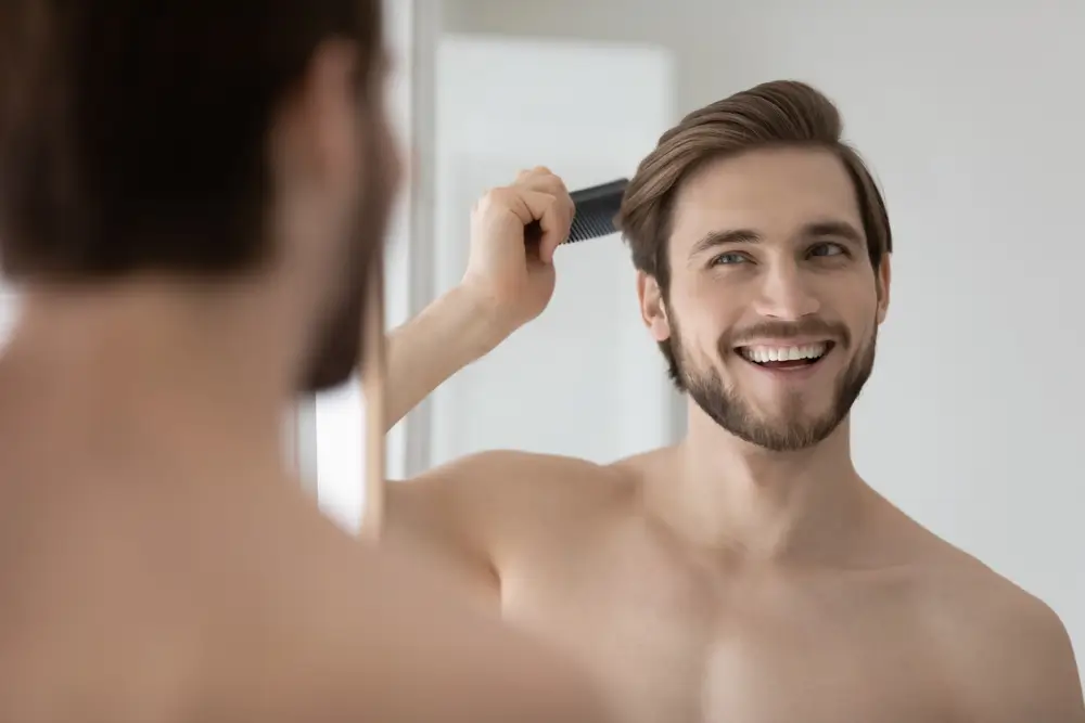 Happy handsome young man combing smooth straight hair after hair transplant